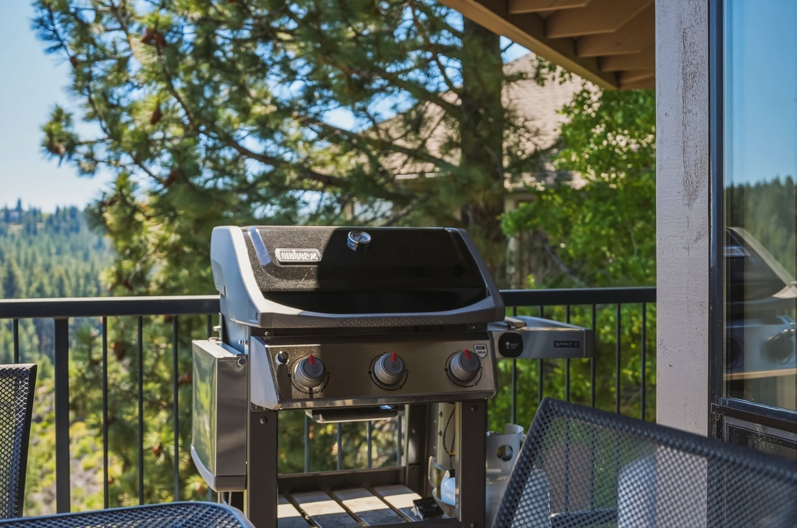 A barbecue grill on a balcony with a view of trees and a mountain.