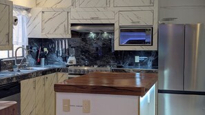 Cozinha moderna com bancadas de mármore, fogão embutido e geladeira de aço inoxidável.