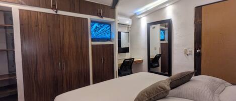 A bedroom with a bed, a ceiling fan, wooden wardrobes, a desk, and a mirror.