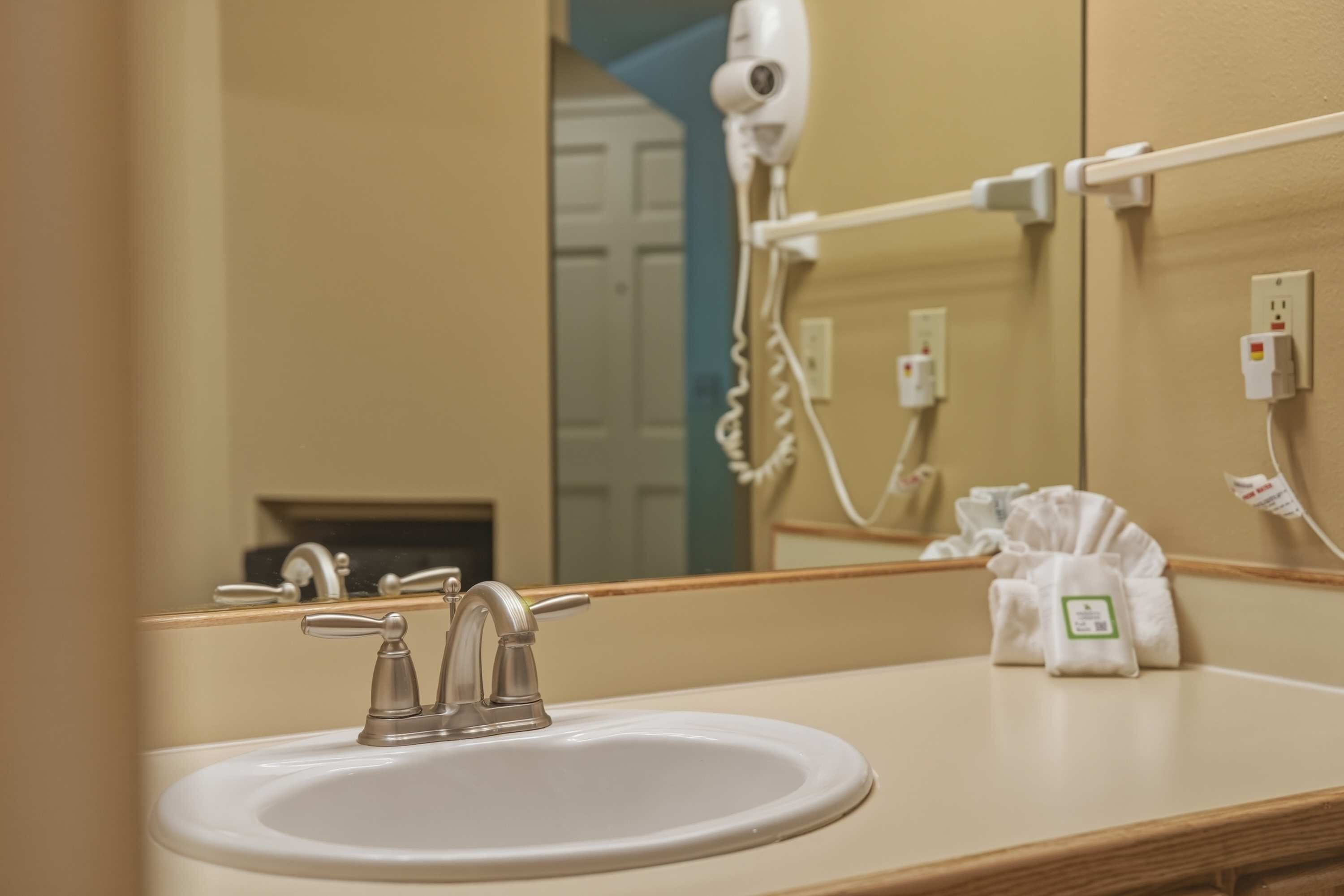 Une salle de bain équipée d’un lavabo, d’un miroir, d’un sèche-cheveux et d’un porte-serviettes.