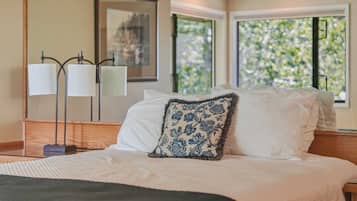 Quarto de hotel com cama, mesa de cabeceira, luminária e janela com vista para áreas verdes.