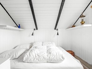 Ein weißes Zimmer mit einem Bett, zwei Wandlampen und einem Regal mit einer blauen Flasche.
