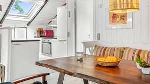 Et spiseområde med et træbord, en kurv med brød og en bænk med stribede hynder.