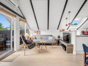 Ein modernes Interieur mit einer Couch, Sesseln, einem Fernseher und einem Grillbereich.