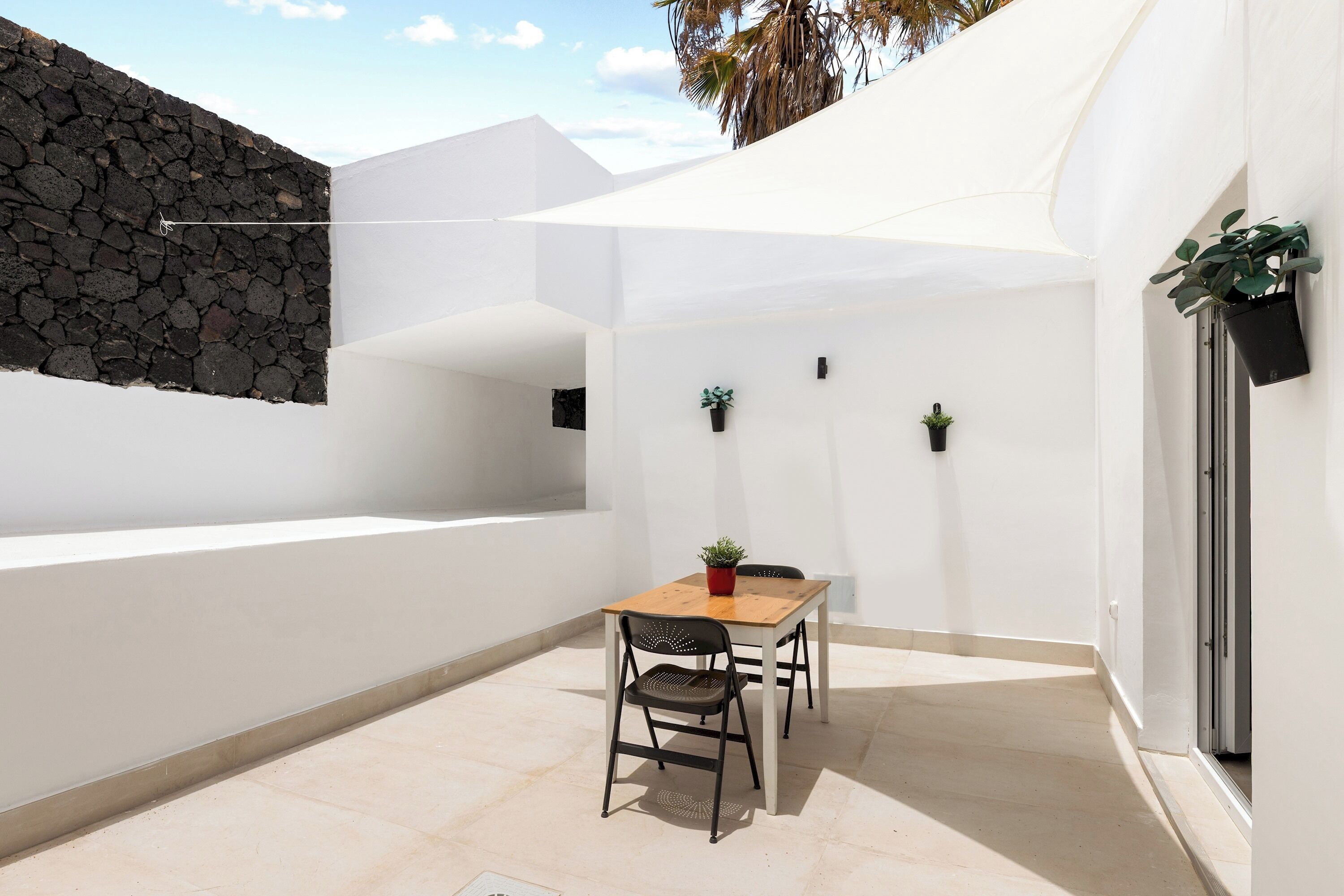 A patio with a table and chairs, a stone wall, and potted plants.