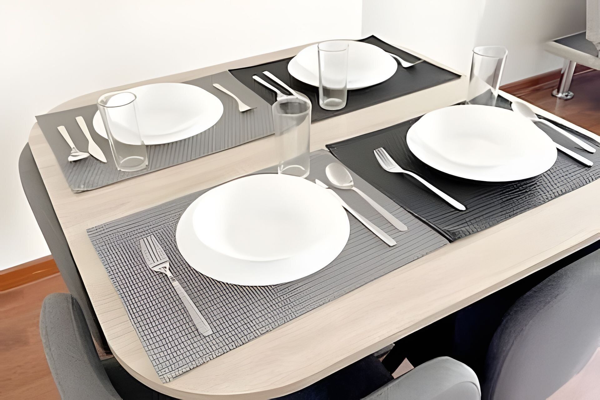 A dining table set with white plates, cutlery, and glasses, with a textured placemat.