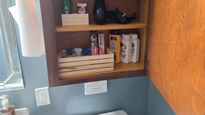 Uma prateleira no banheiro com artigos de higiene pessoal, incluindo uma garrafa verde, um vaso preto e diversos produtos de cuidados.