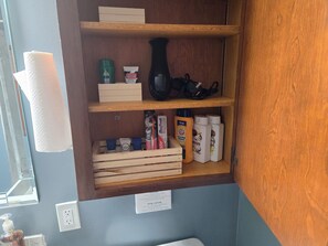 A bathroom shelf with toiletries including a green bottle, a black vase, and various personal care products. - Cozy 3 BDRM Home 3 minutes to Arrowhead & Kauffman Stadium (Kansas City)