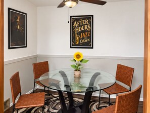 A dining area with a glass table surrounded by leather chairs, a sunflower centerpiece, and a poster on the wall.