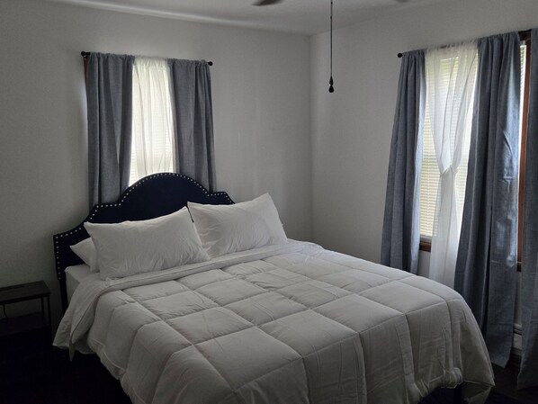 A bedroom with a bed, curtains, and a hanging light fixture.