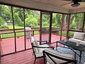 A covered outdoor deck with a red railing, a table, chairs, and a ceiling fan.