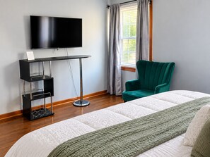 A hotel room with a bed, a TV mounted on the wall, a desk with a chair, and a window with curtains.