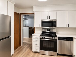A modern kitchen with stainless steel appliances, white cabinetry, and a wooden floor.