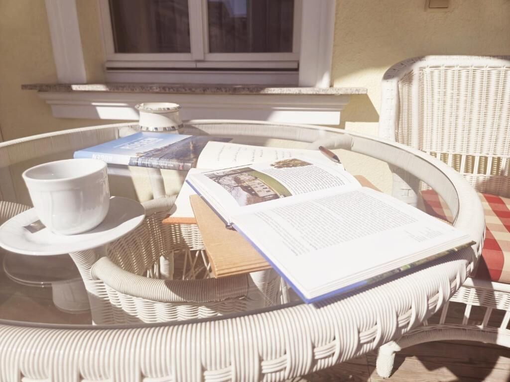 Un tavolino rotondo in vimini con piano in vetro, una tazza bianca, un libro e una rivista.