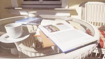 Un tavolino rotondo in vimini con piano in vetro, una tazza bianca, un libro e una rivista.