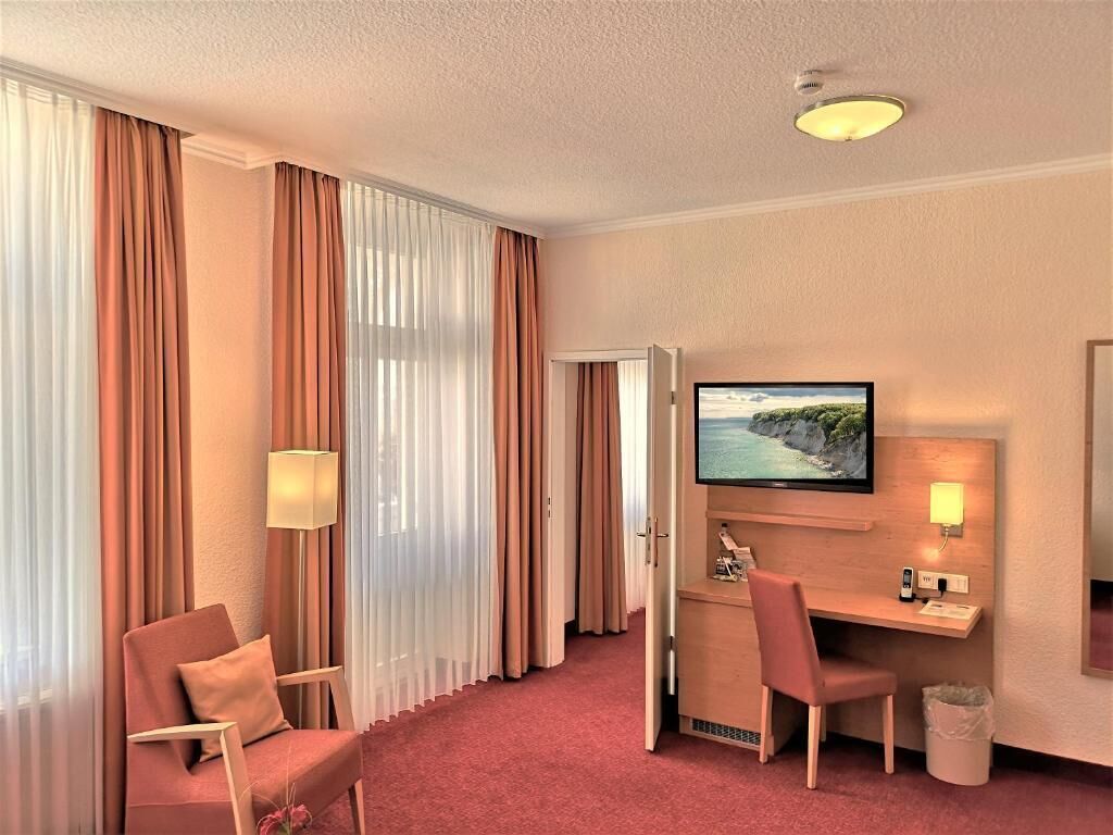 Habitación de hotel con cama, escritorio, computadora, televisor, silla y lámpara.