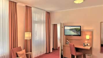 Habitación de hotel con cama, escritorio, computadora, televisor, silla y lámpara.