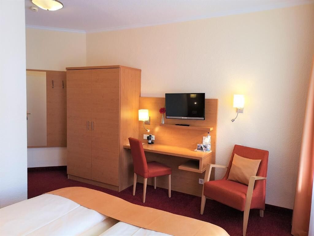 Een hotelkamer met een bed, een bureau, twee stoelen, een televisie en een kledingkast.
