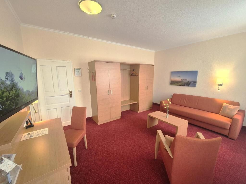 A room with a red carpet, a sofa, a TV, a desk, and a wardrobe.