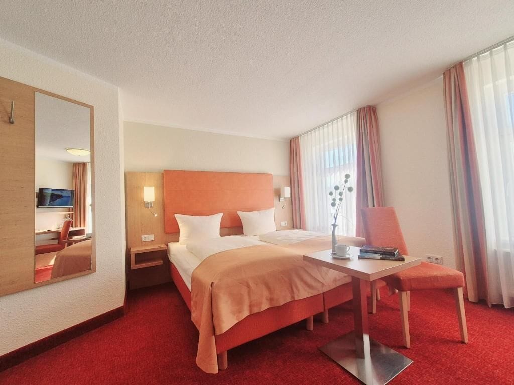 Une chambre d’hôtel équipée d’un lit, d’un bureau, d’une chaise, d’une télévision et d’un grand miroir.