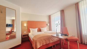 Une chambre d’hôtel équipée d’un lit, d’un bureau, d’une chaise, d’une télévision et d’un grand miroir.