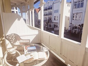 A balcony with a wicker chair, a glass table with books and a cup, and a view of buildings. - Villa Meeresgruss (Binz)