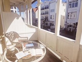 Ein Balkon mit einem Korbstuhl, einem Glastisch mit Büchern und einer Tasse, und Blick auf Gebäude.