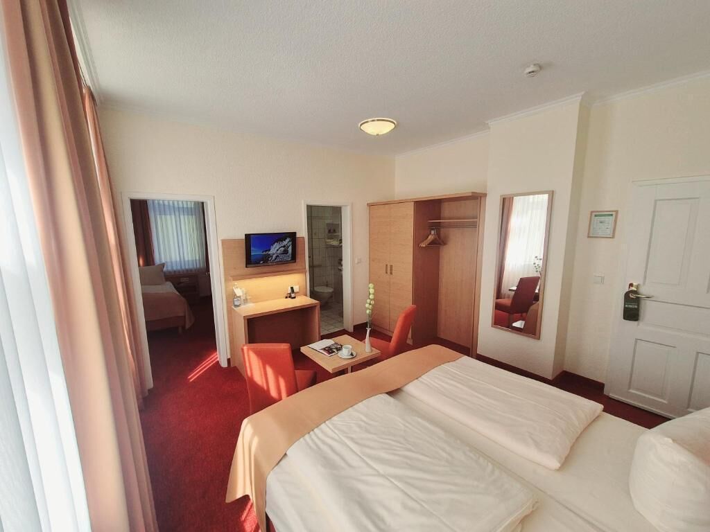 A hotel room with a bed, a desk, a chair, a television, a wardrobe, and a door.