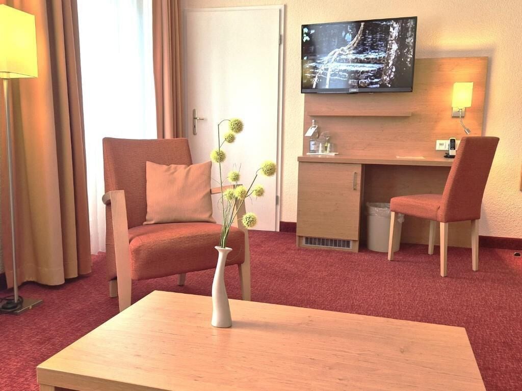 Une chambre d’hôtel avec un canapé, une petite table sur laquelle est posé un vase, un bureau avec une chaise, une télévision et une lampe.