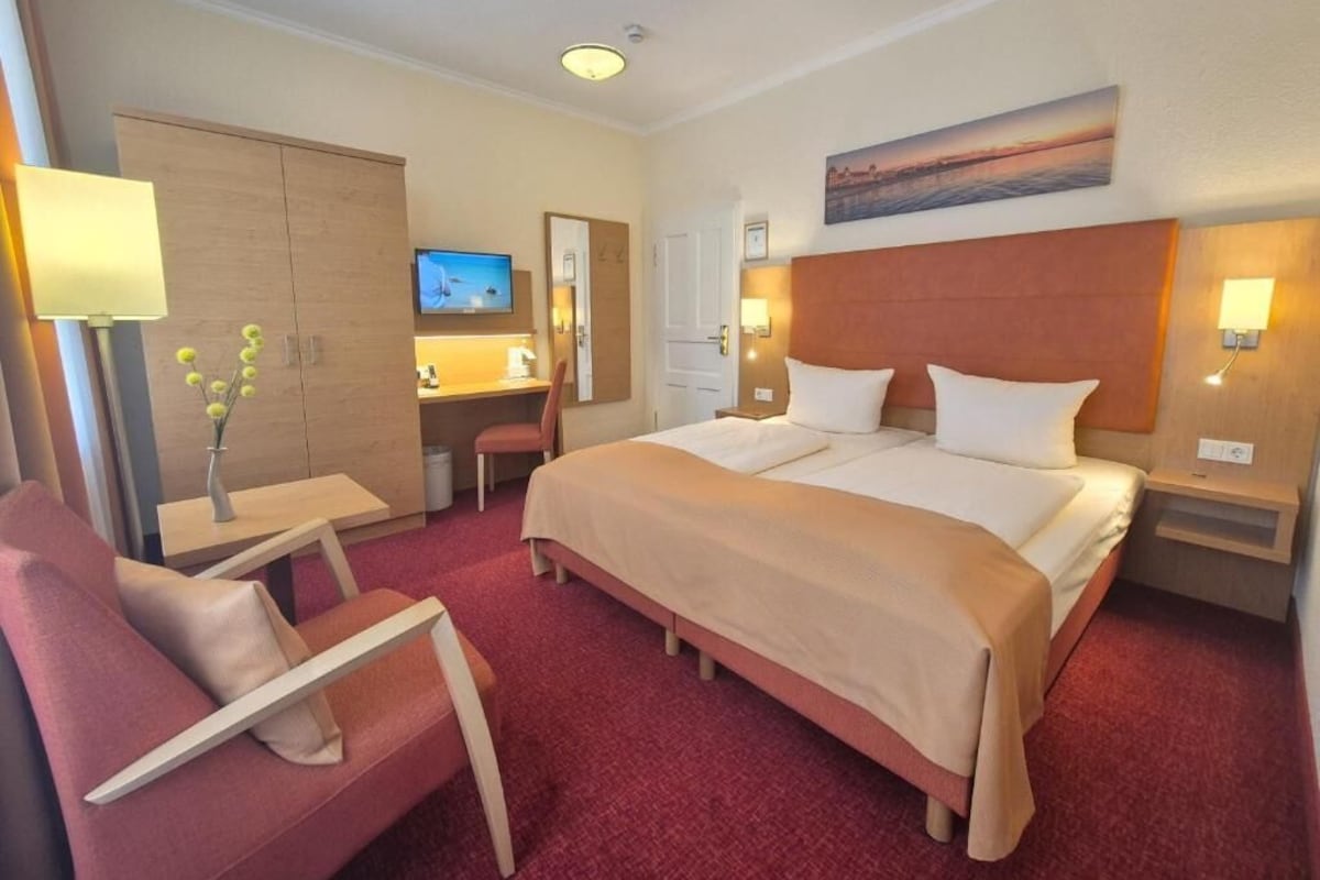 Habitación de hotel con cama, escritorio, silla, televisor y un cuadro en la pared.