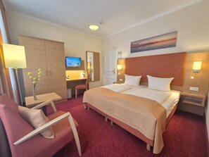 A hotel room with a bed, a desk, a chair, a TV, and a painting on the wall. - Villa Meeresgruss (Binz)