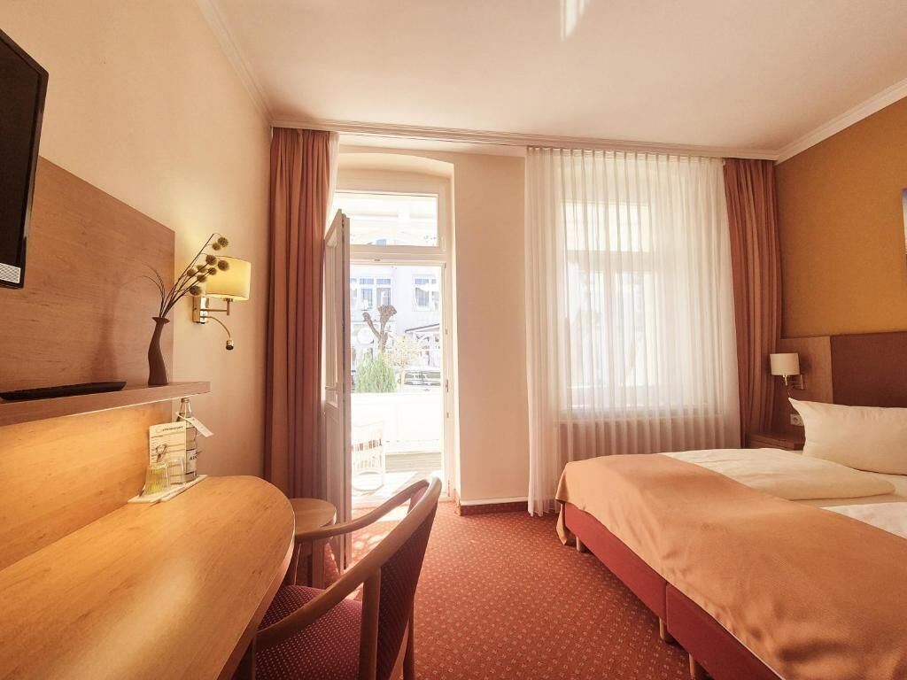 Hotellihuone, jossa on sänky, työpöytä, tuoli, lamppu ja ikkunasta avautuva näkymä ulos.
