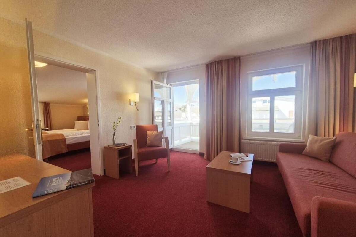 Habitación de hotel con cama, sofá, mesa de centro, silla y escritorio. Cuenta con ventana con cortinas y vistas al exterior.
