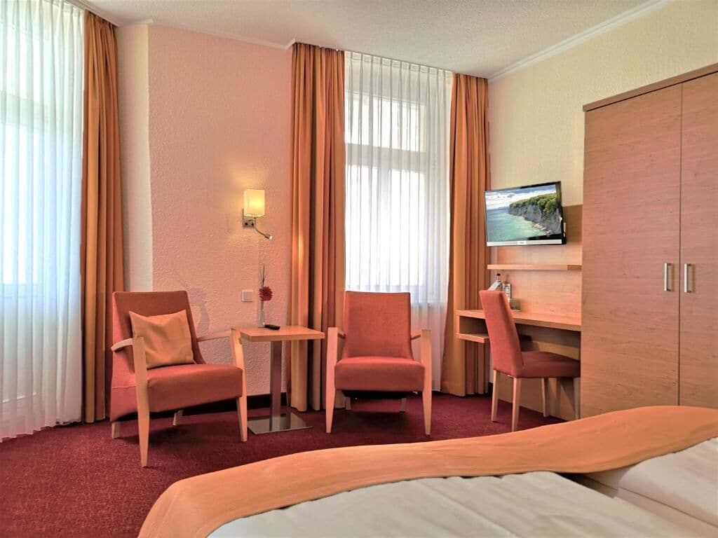 Quarto de hotel com cama, duas poltronas, uma mesinha, televisão e guarda-roupa.