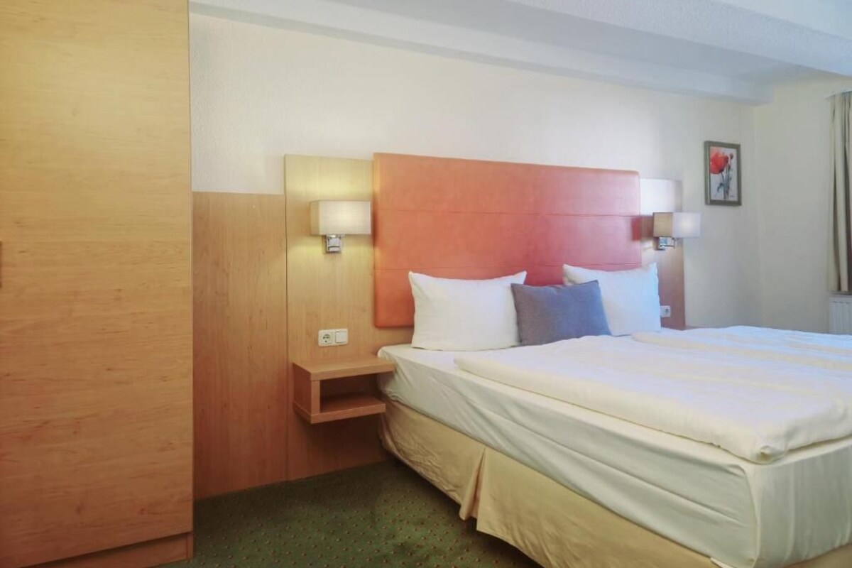 Una habitació d'hotel amb un llit, làmpades de nit, un armari de fusta i una petita taula de nit.