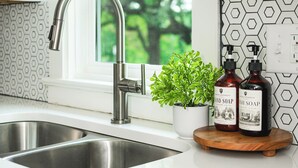 Un lavamanos de cocina con un grifo moderno, una planta en maceta y dos botellas de jabón de manos sobre una bandeja de madera.