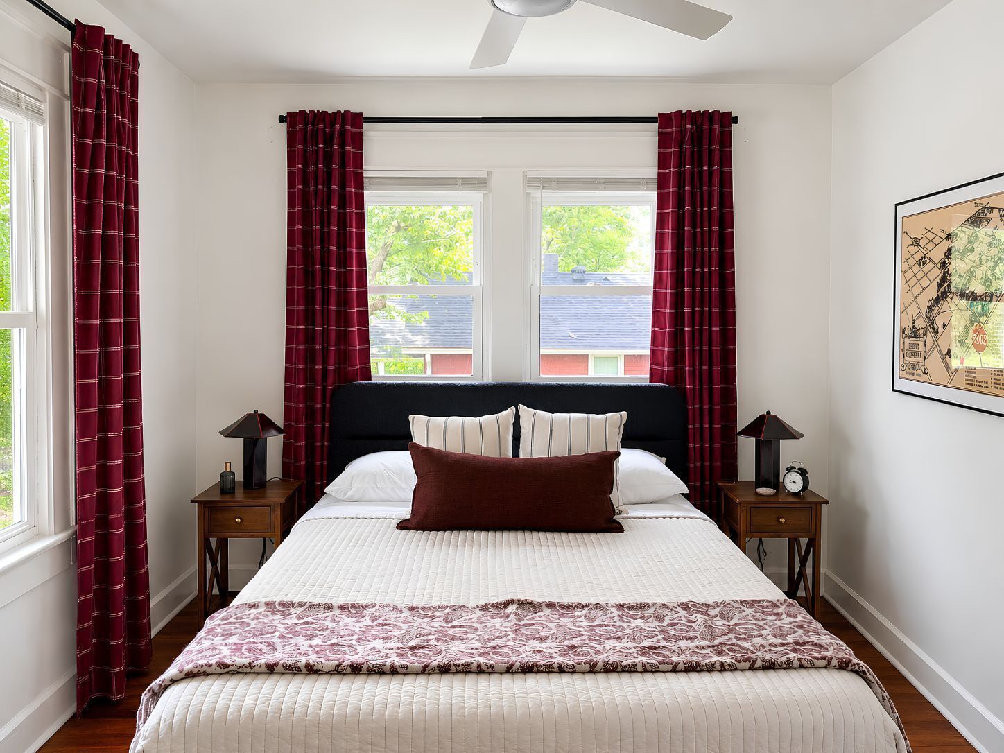 Une chambre à coucher avec un lit, deux tables de chevet, un ventilateur de plafond et une fenêtre avec des rideaux.