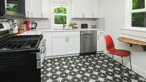 A modern kitchen with white cabinets, a black and white patterned floor, a red chair, and a window with a view of greenery. - Located in the IU Tailgate Fields - Across from Memorial Stadium (Bloomington)