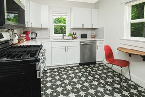 A modern kitchen with white cabinets, a black and white patterned floor, a red chair, and a window with a view of greenery. - Located in the IU Tailgate Fields - Across from Memorial Stadium (Bloomington)