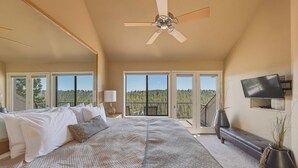 A bedroom with a large bed, a ceiling fan, a TV, and a balcony with a view of trees. - River Ridge at Mt Bachelor A (Bend)