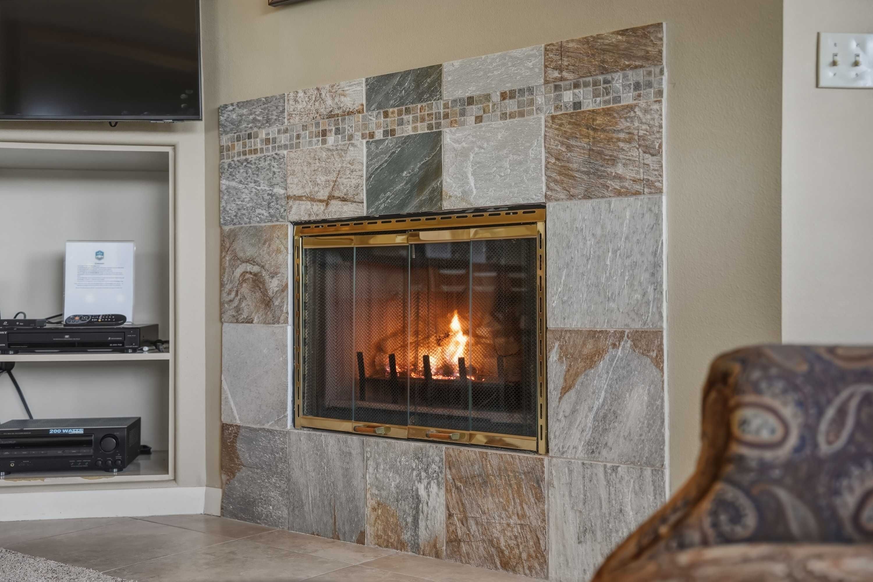 Una chimenea con un revestimiento de piedra, un televisor montado encima y un estante con dispositivos electrónicos.