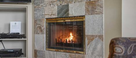 Una chimenea con un revestimiento de piedra, un televisor montado encima y un estante con dispositivos electrónicos.