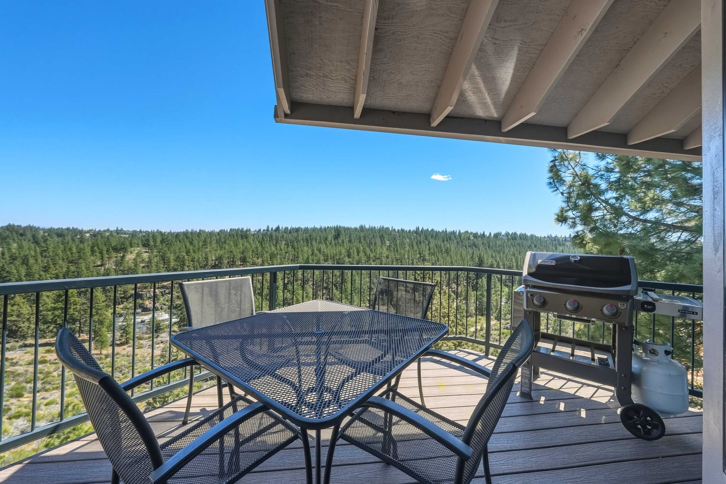 A deck with a table and chairs, a grill, and a view of a forested area.