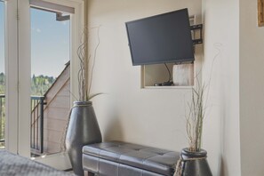 Ein Zimmer mit an der Wand montiertem Fernseher, einer Bank und zwei großen Vasen mit Pflanzen.