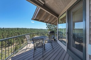 A balcony with a table and chairs, a grill, and a view of a forested area. - River Ridge at Mt Bachelor A (Bend)