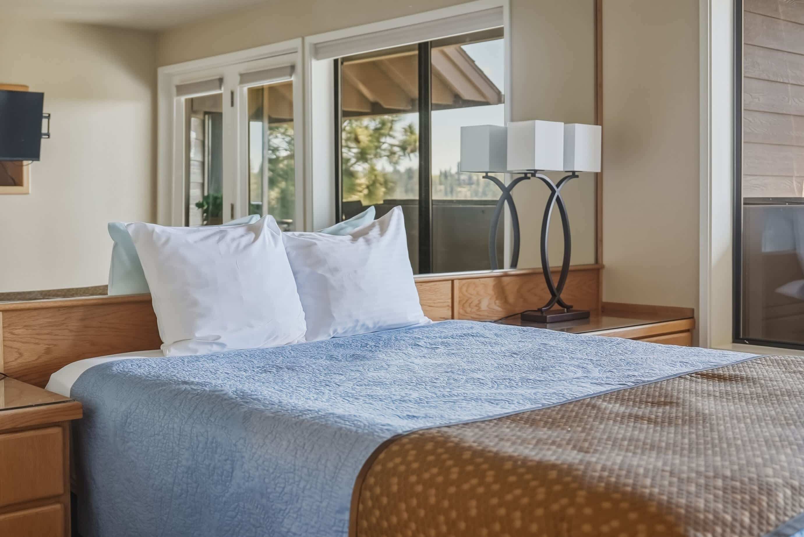 Camera d'albergo con un letto, un comodino, una lampada e una finestra vista palme.
