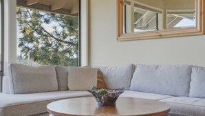 A living room with a sectional sofa, a round wooden coffee table, and a large window with a view of trees. - River Ridge at Mt Bachelor A (Bend)