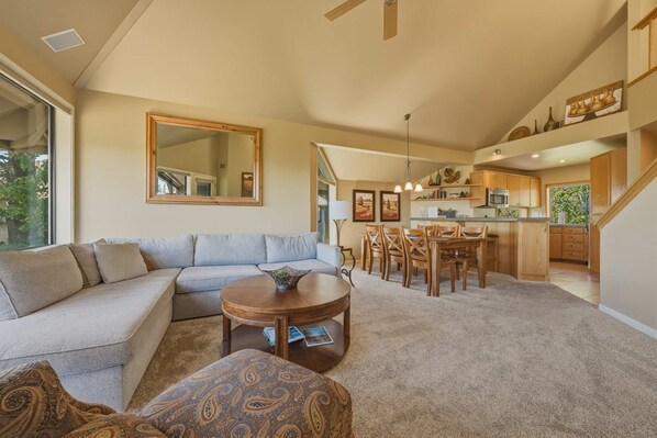 A living room with a sofa, a coffee table, and a dining area with chairs and a kitchen in the background. - River Ridge at Mt Bachelor A (Bend)
