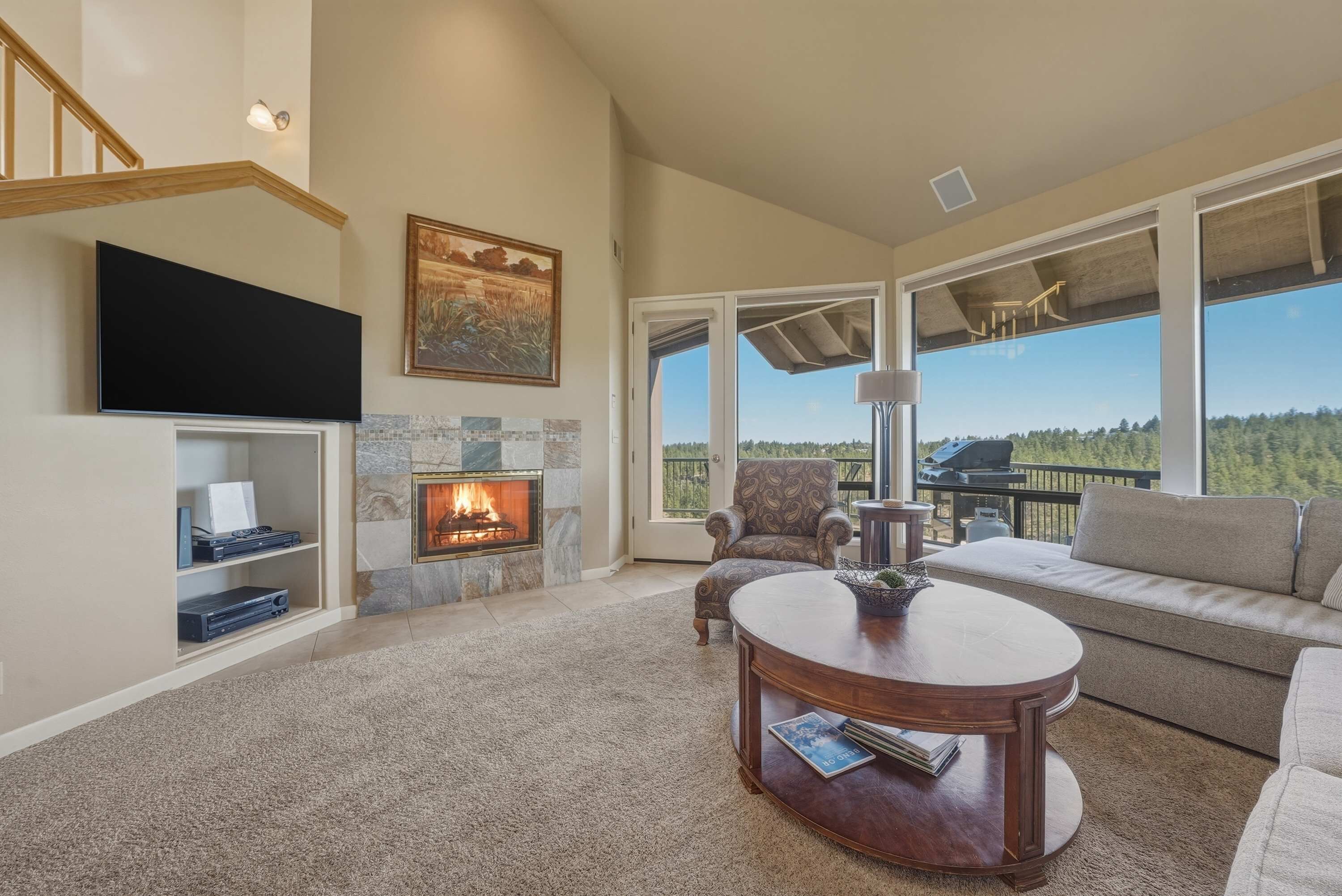 A living room with a fireplace, a television, a sofa, and a large window with a view.
