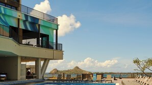 A swimming pool with lounge chairs, a building with balconies, and a clear sky.